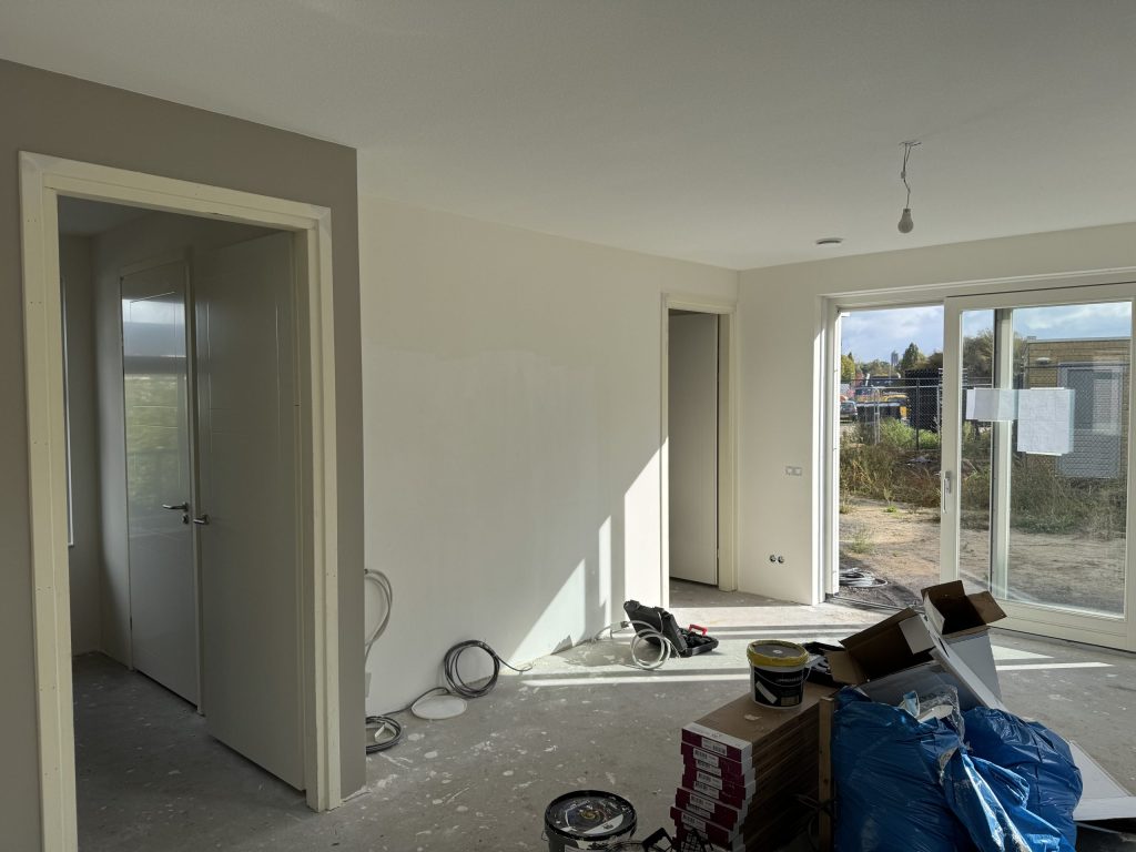 Woonkamer van een eengezinswoning tijdens de afwerking, met tuindeuren en materiaal op de vloer