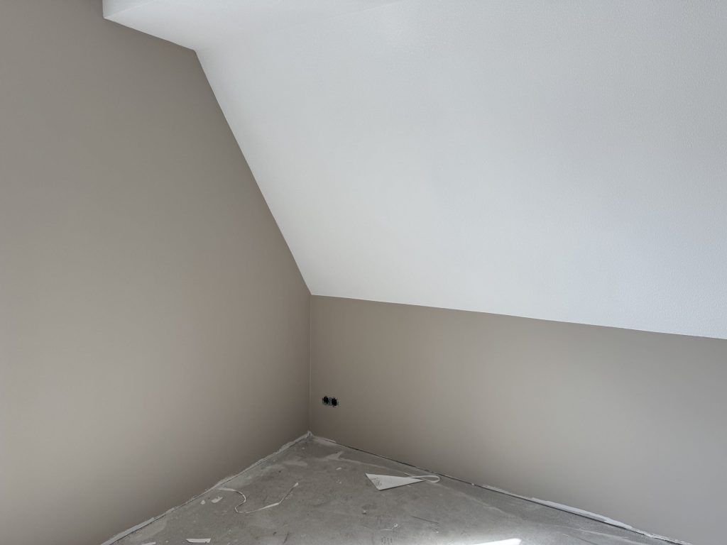 Zolderkamer met een schuin dakvlak en een wit plafond boven grijs gesausde wanden