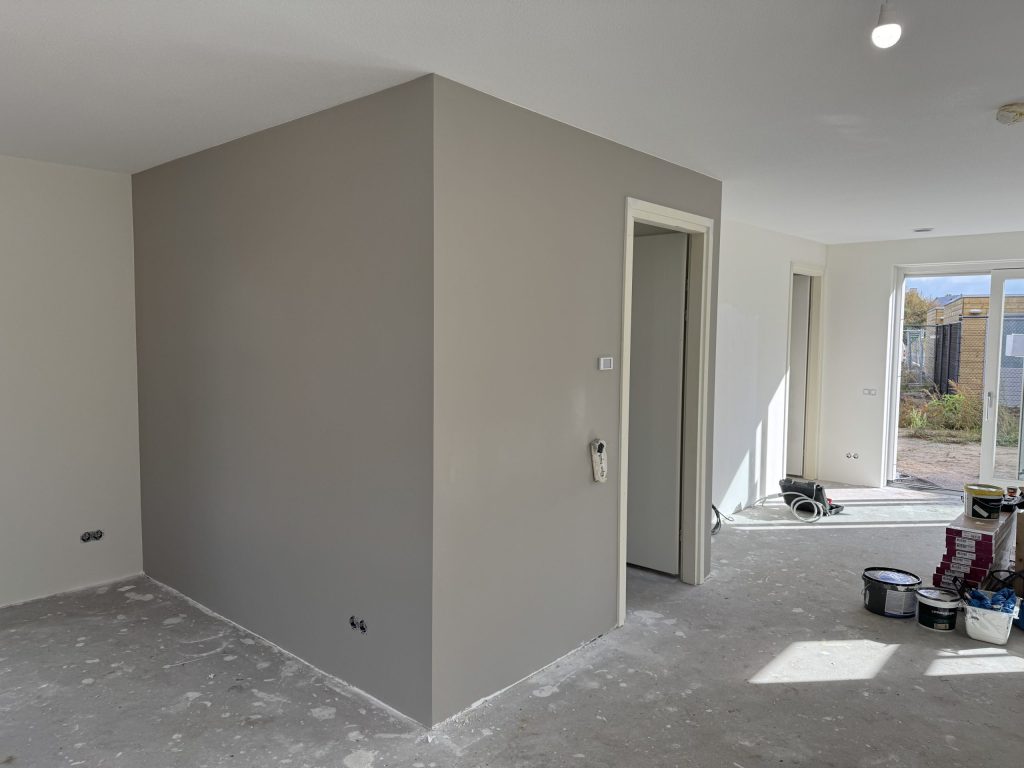 Woonkamer met een pas afgewerkte grijze wand en verfemmers op de vloer