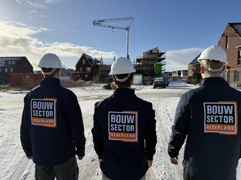 Drie vakmensen van Bouwsector Nederland met witte helm op een besneeuwde bouwplaats